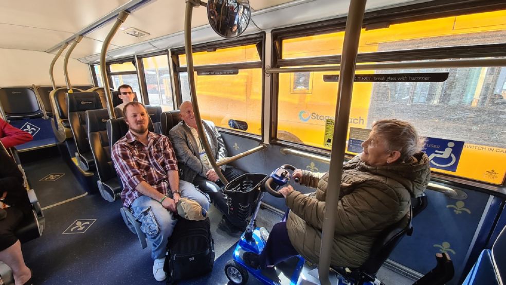 people sat on a bus including a woman in a mobility scooter