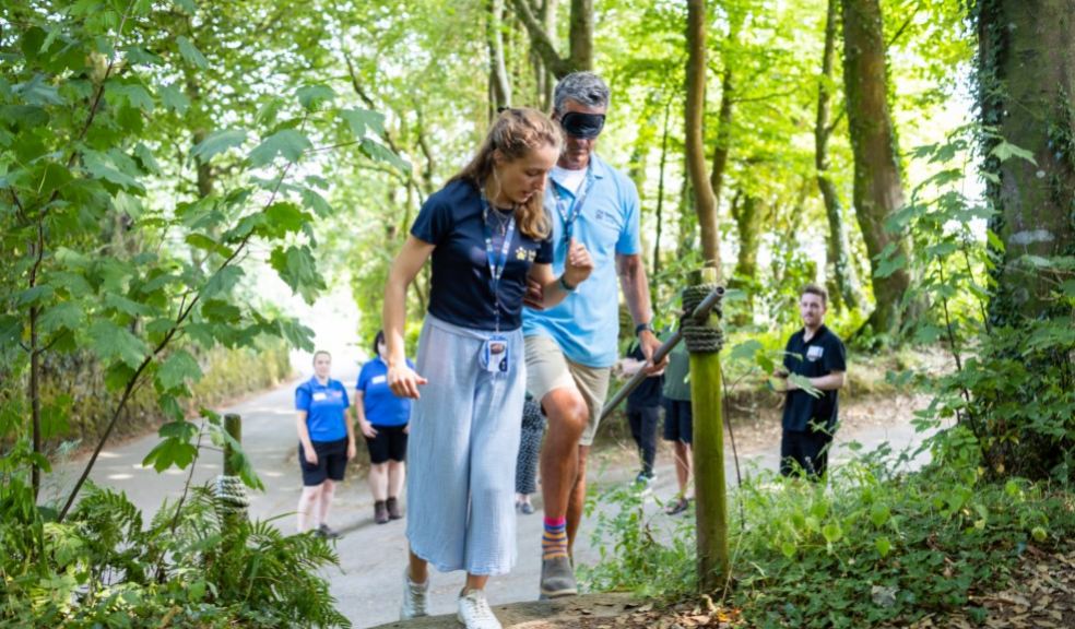 Two staff members from Guide Dogs demonstrate how to guide someone up a set of steps. They are outdoors in the Zoo grounds surrounded by greenery. Two staff members from Guide Dogs demonstrate how to guide someone up a set of steps. They are outdo
