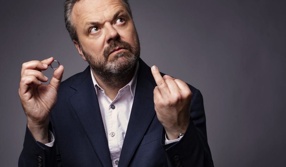 A photo of Hal Cruttenden wearing a blue suit and holding his wedding ring 