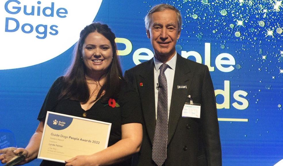 Lynda Palmer with her award standing with Jamie Hambro, Guide Dogs Chairman