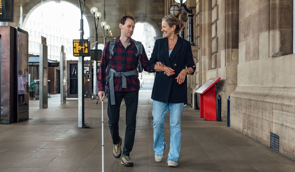 Celebrate travel heroes Visually impaired man with white walking aid walking through a station with a woman