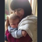 A mother lovingly cuddles her baby son with her hand cradling his head. Both have eyes closed.