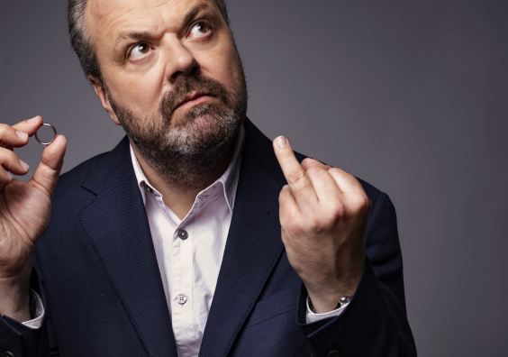 A photo of Hal Cruttenden wearing a blue suit and holding his wedding ring 