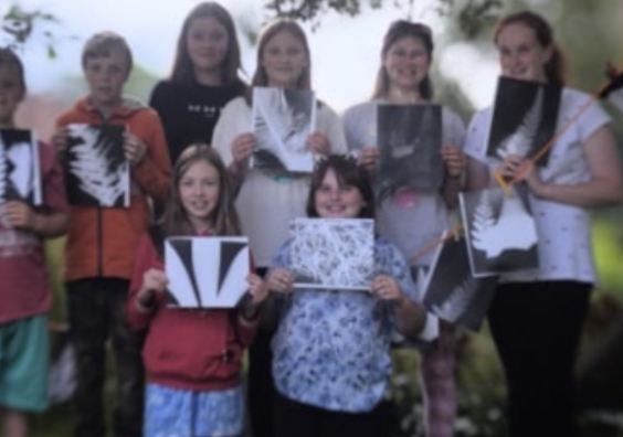 Teen holding up their art for photo in forest