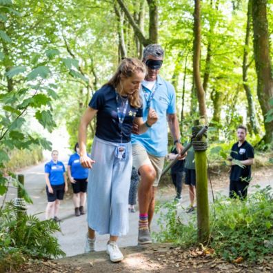 Two staff members from Guide Dogs demonstrate how to guide someone up a set of steps. They are outdo