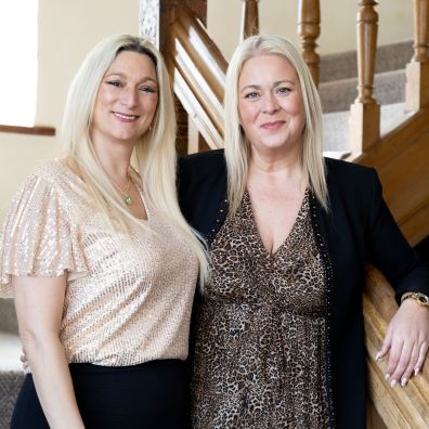 Owners, Cristina Axford (left) and Jo Lines (right) stand on stairs, smiling