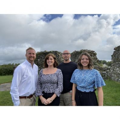 Four people standing next to each other, outside.  