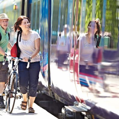 A man and a woman wheel bikes along a station platform beside a stationary train