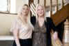 Owners, Cristina Axford (left) and Jo Lines (right) stand on stairs, smiling