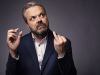 A photo of Hal Cruttenden wearing a blue suit and holding his wedding ring 